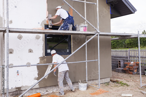 Workers spreading mortar over styrofoam insulation and mesh with trowel photo