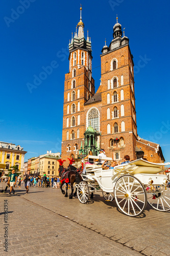 Church of St. Mary in the main Market Square with beautifully decorated horse and white old coach in the foreground. Basilica Mariacka. Krakow. Poland.