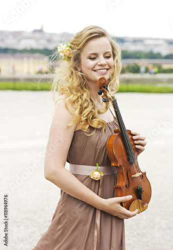 Beautiful smiling girl with a violin outdoor.Beautiful smiling girl playing on the violin outdoors. Musician for the wedding.Violin under the open sky 