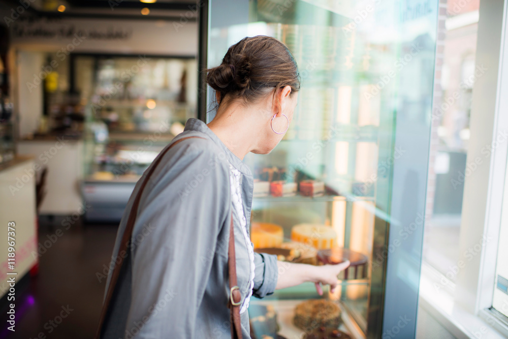Rear view of brunette woman pointing at pie in showcase