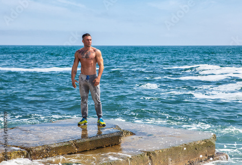 Man Athlete stands on a rock by the sea against the sky