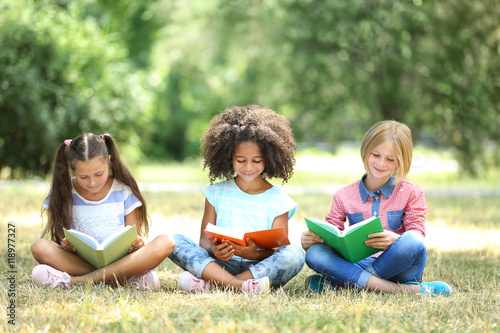 Cute kids reading books on green grass