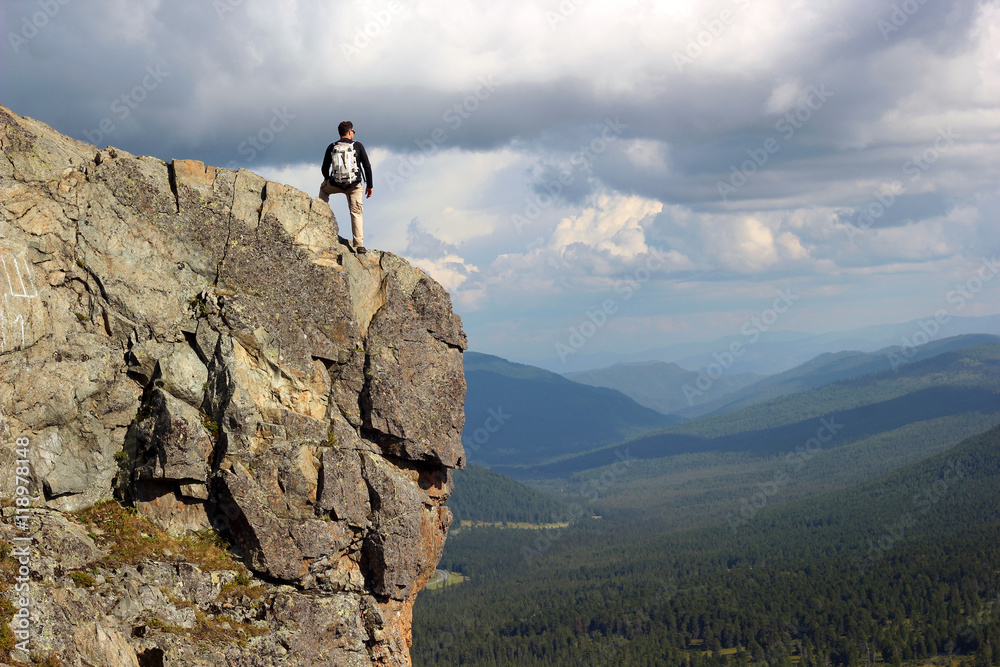 Hiker with backpack standing on top off high rocks. Tourism conc