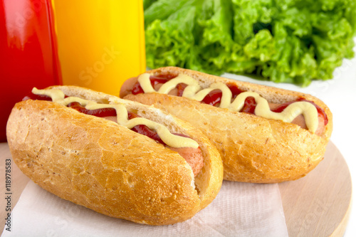 Hotdog with bottle of mustard and ketchup with salad on wooden d