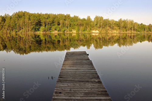 Wooden pier by the river and the forest reflected in water.