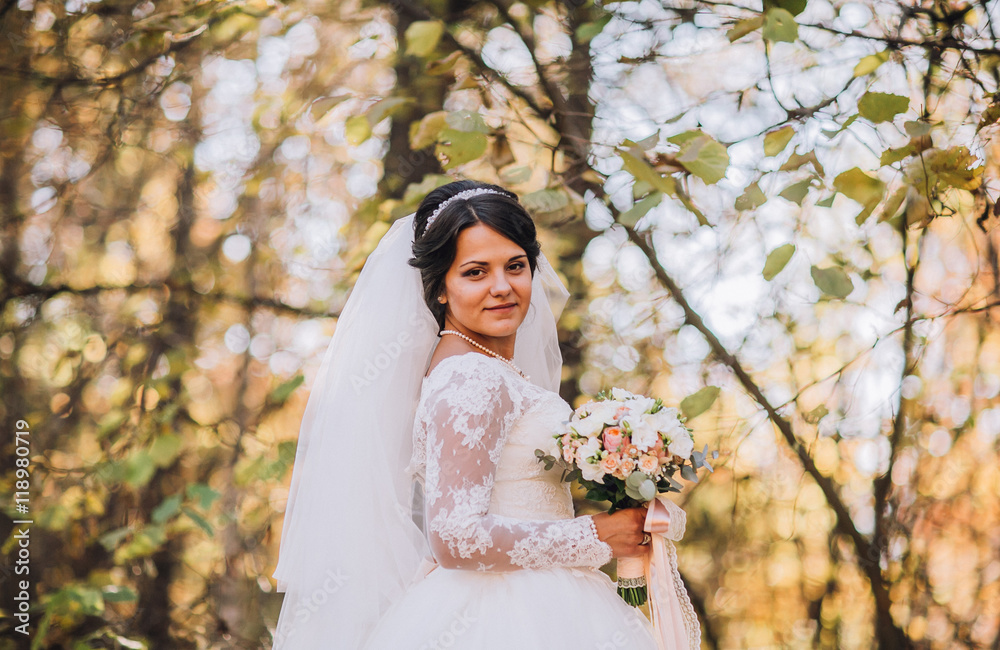 Gorgeous blonde bride in wedding dress with fallen leaves bouquet posing in sunny autumn park/Happy Beautiful young bride in white dress sitting in autumn park among fallen leaves Gorgeous blonde bride in wedding dress with fallen leaves bouquet posing in sunny autumn park/Happy Beautiful young bride in white dress sitting in autumn park among fallen leaves