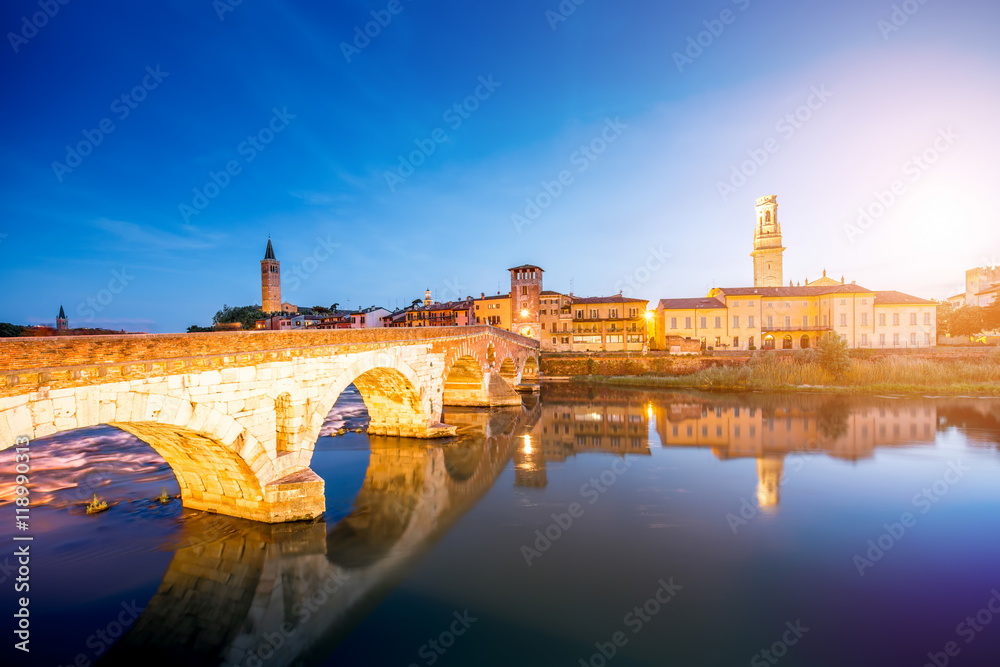 Verona cityscape view on the illuminated riverside with historical buildings and towers on the sunset