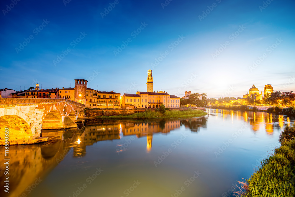 Verona cityscape view on the illuminated riverside with historical buildings and towers on the sunset