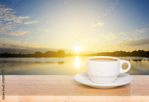 white coffee cup on wood table and view of sunset in the river background