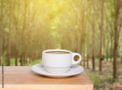 Wooden table top and coffee cup on blurred para rubber tree