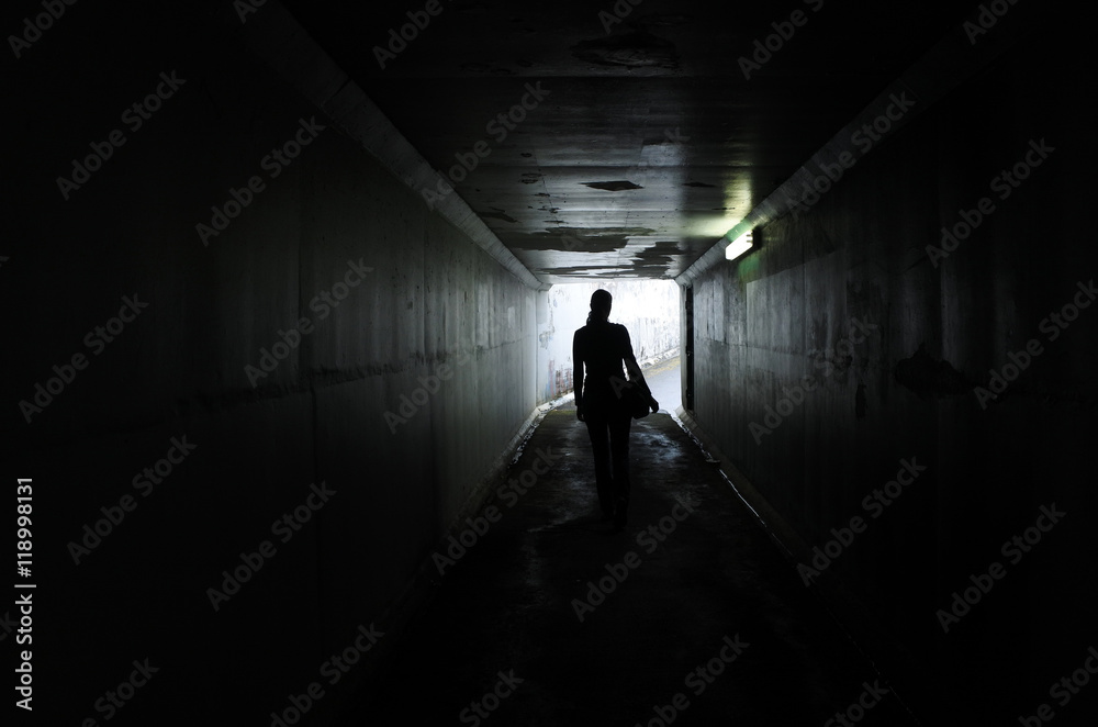 Silhouette of a young woman walks alone in a dark tunnel Silhouette of a young woman walks alone in a dark tunnel