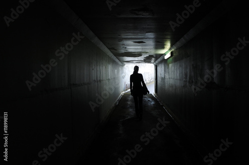 Silhouette of a young woman walks alone in a dark tunnel photo