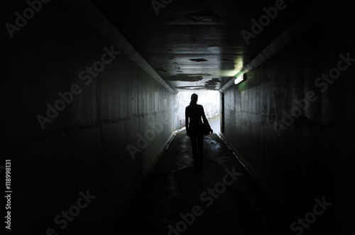 Silhouette of a young woman walks alone in a dark tunnel