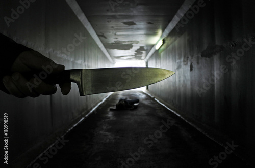 Man hand holds a knife over a murder victim in a dark tunnel