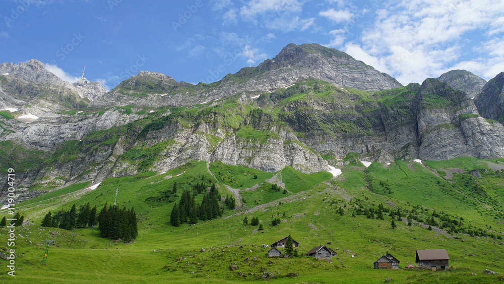 Schweizer Berge/Das Alpsteinmassiv in den Schweizer Bergen, grüne Bergwiesen mit kleinen Hütten, blauer Himmel und weiße Wolken 