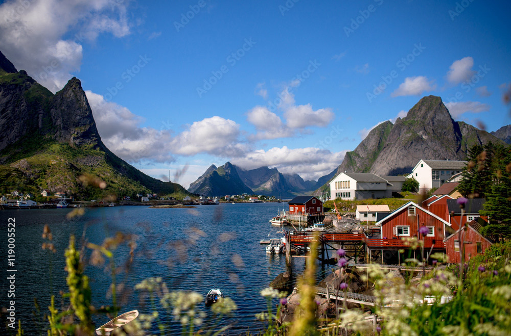 Reine in Lofoten Islands, Norway, with traditional red rorbu huts under blue sky with clouds. 