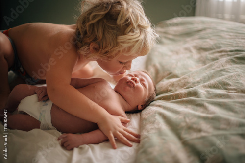 Big brother kissing baby on bed 