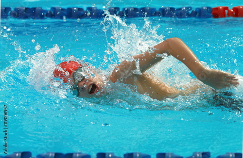 Fototapeta Boy swimmer wearing red cap swim freestyle swimming stroke in a swimming pool