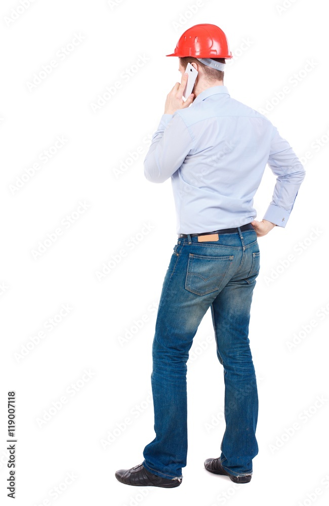 Backview of business man in construction helmet stands and enjoys tablet or using a mobile phone. businessman in a white shirt and a construction helmet on the phone. Backview of business man in construction helmet stands and enjoys tablet or using a mobile phone. businessman in a white shirt and a construction helmet on the phone.