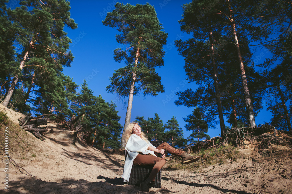 Fototapeta premium happy woman sitting in a chair on a sandy cliff in the forest