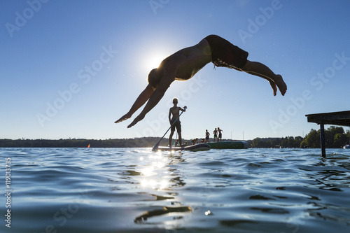Mann springt vom Steg in den See