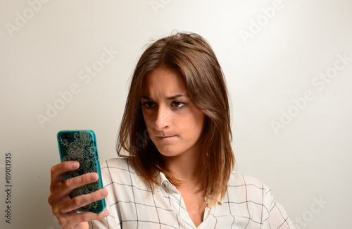 junge Frau schaut verärgert mit verkniffenem Mund und Zornfalte auf ihr Handy