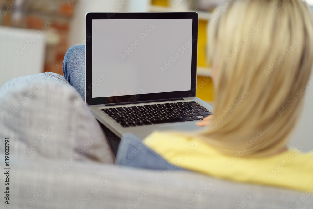 Fototapeta premium frau sitzt auf der couch und schaut auf ihren laptop