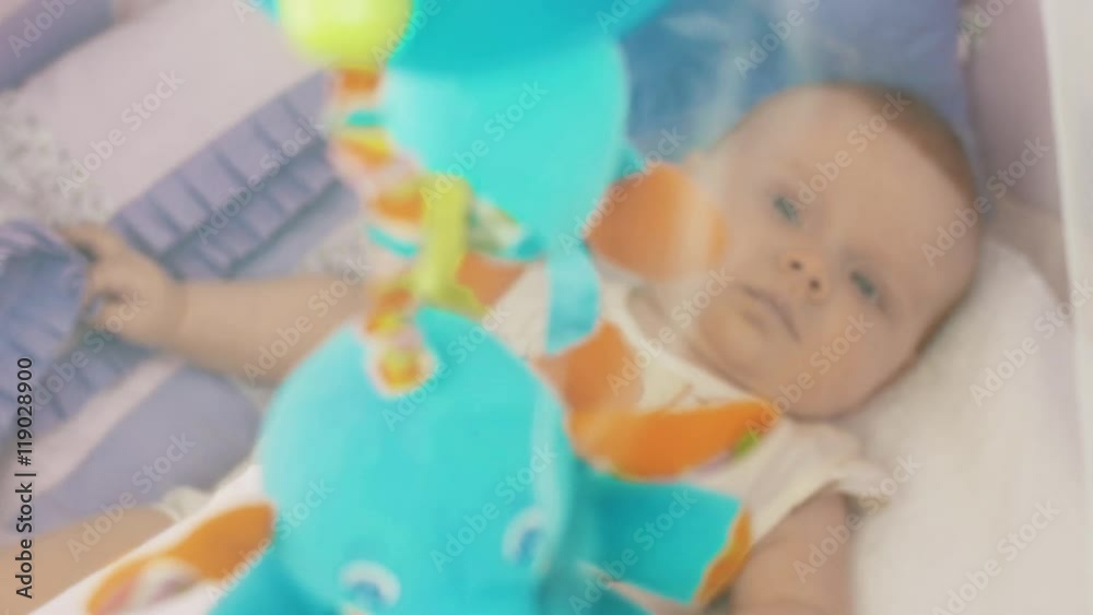 Little baby lie in crib watching moving colorful toys. Motherhood. Mothering. Happiness Little baby lie in crib watching moving colorful toys. Motherhood. Mothering. Happiness