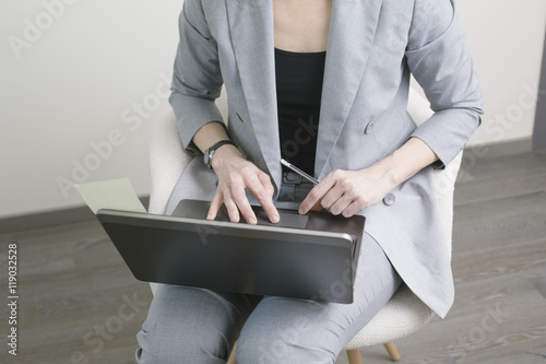 Business woman typing on the laptop on the knees with pencil in her hand in the office. Close-up hands
