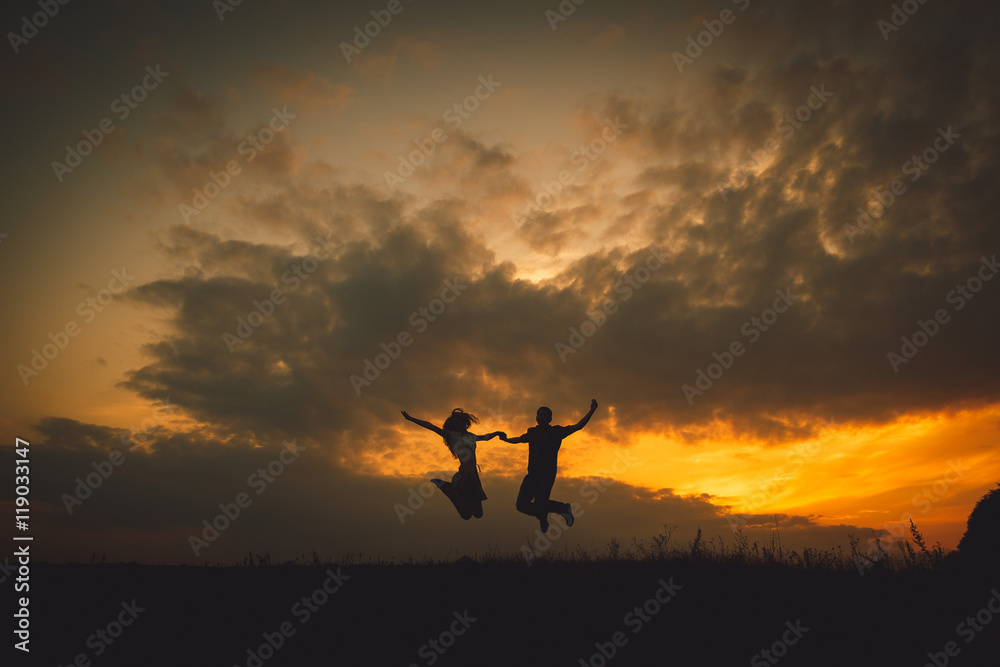 Young couple hold their hands tightly while jumpung under golden Young couple hold their hands tightly while jumpung under golden
