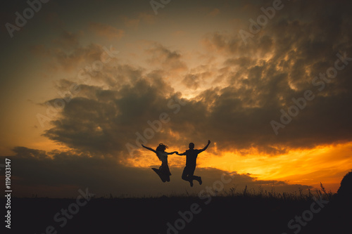 Young couple hold their hands tightly while jumpung under golden