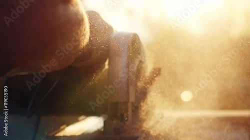 Man is craft working at a work bench with power tools in slowmotion during sunset with beautiful lens flare. 1920x1080 photo