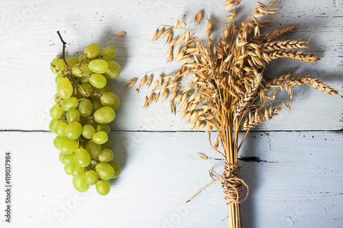 White grape, green apple, ears of oat and wheat on wooden, blue background