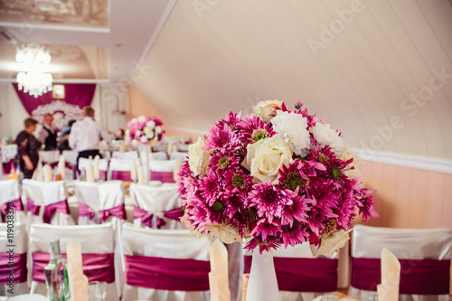 Dark pink bouquet stands in white vase on the rich dinner table