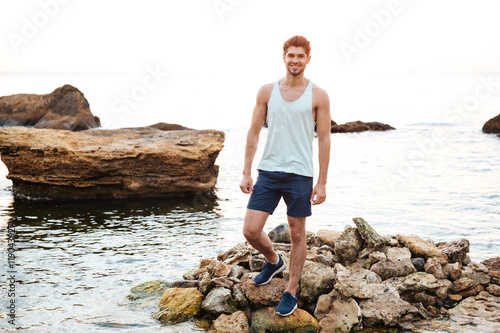 Young handsome man athlete standing at the rocky beach