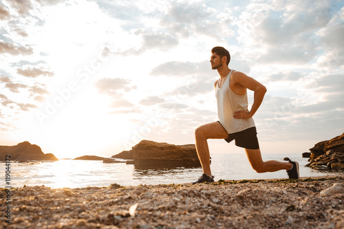 Young healthy man athlete doing squats at the beach photo