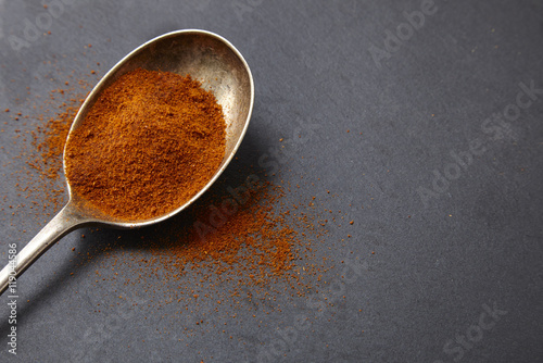 An antique silver spoon full of chili powder seasoning on a rustic slate background forming a page border