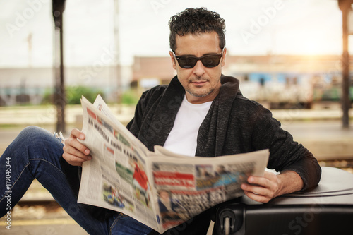 Man sitting on railway platform reading newspaper