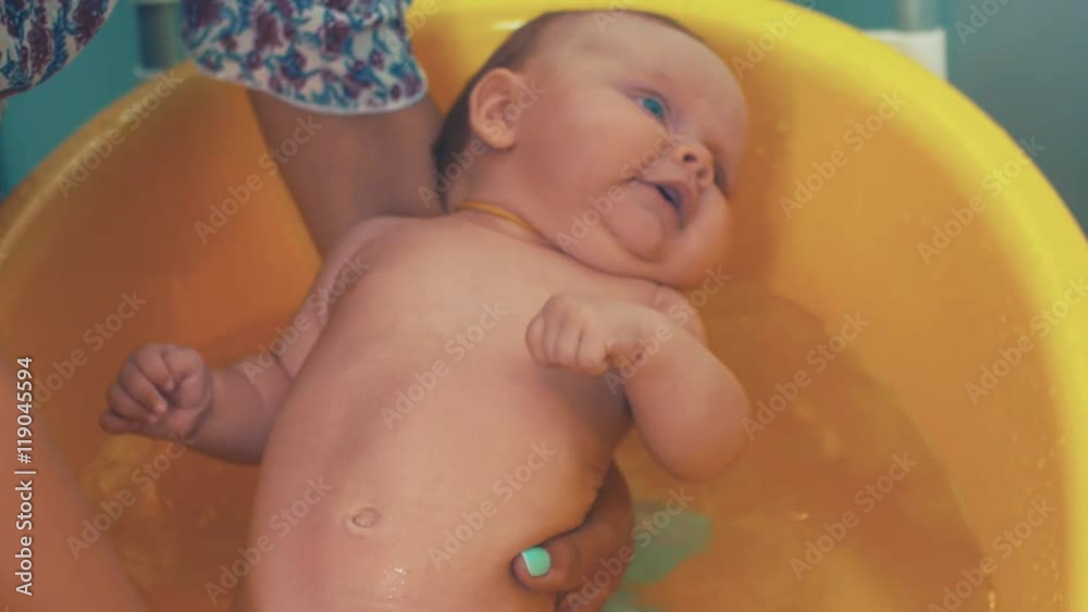 Mother bathing little cute baby with blue eyes. Yellow bath. Motherhood. Communication. Mother bathing little cute baby with blue eyes. Yellow bath. Motherhood. Communication.