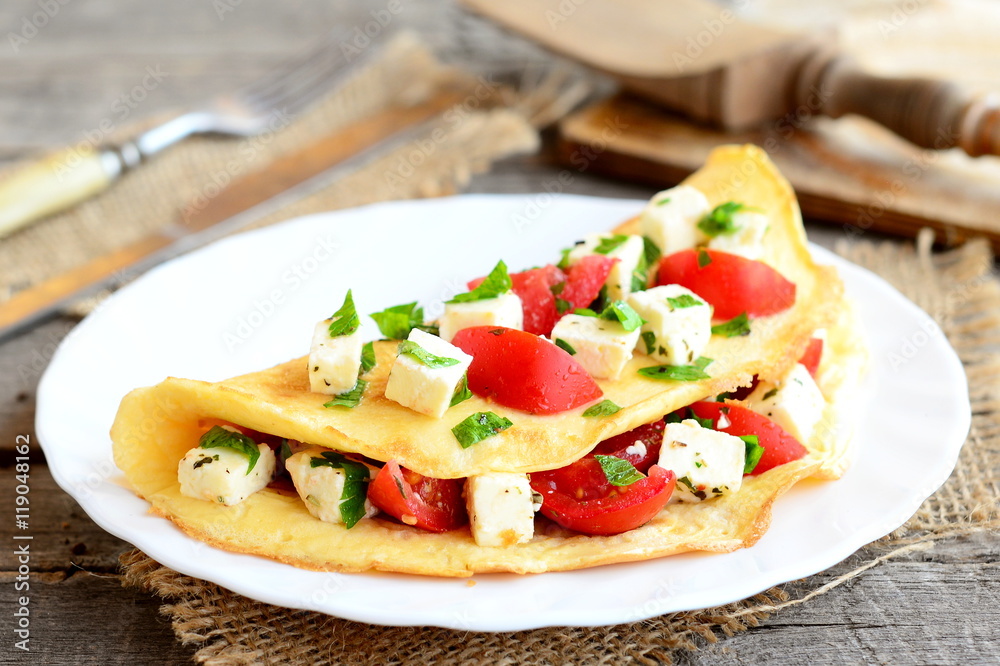 Home stuffed omelet on a plate. Egg omelet with a filling of fresh cherry tomatoes, cheese and parsley. Simple vegetarian breakfast recipe. Fork, knife, cutting board on wooden background. Closeup