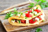 Delicious stuffed omelette on a wooden board. Fried egg omelette with a filling of cherry tomatoes, cheese and parsley. Easy cooking breakfast. Fork, knife, parsley sprigs on wood background. Closeup