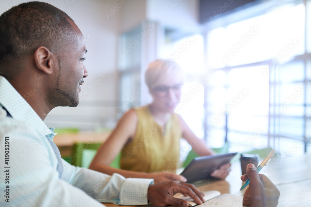 Two creative millenial small business owners working on social media strategy using a digital tablet while sitting at desk Two creative millenial small business owners working on social media strategy using a digital tablet while sitting at desk