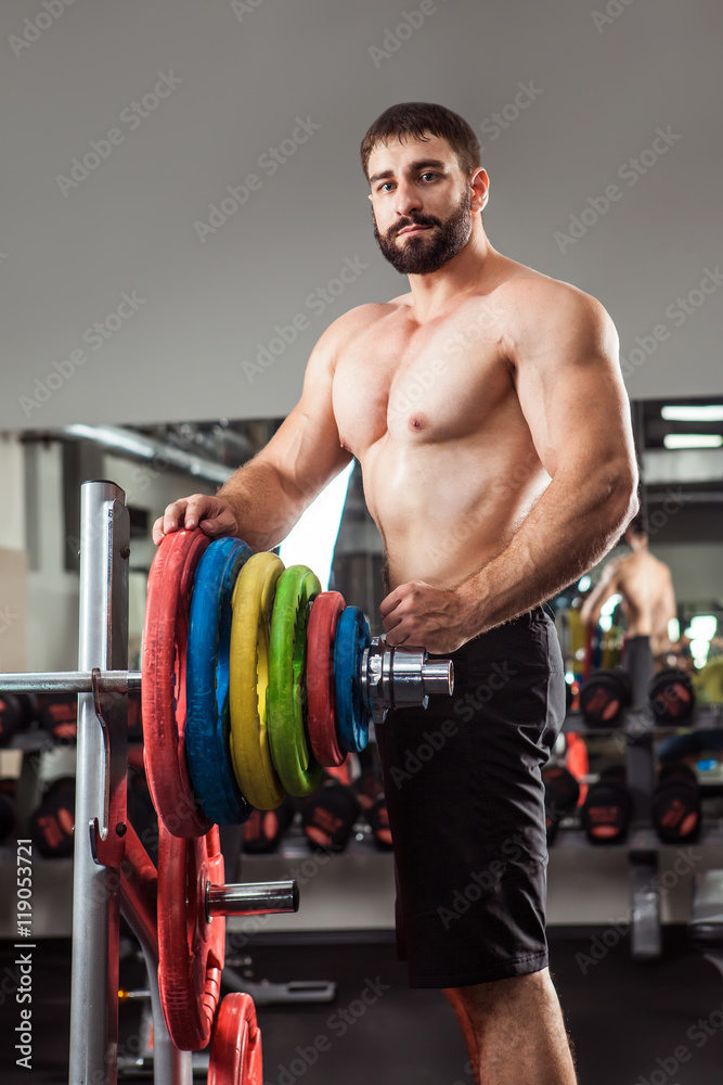 Powerful man with muscular build is standing near the barbell in
