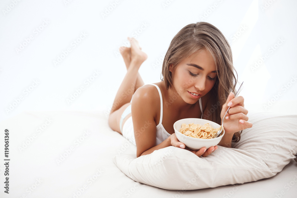Young beautiful girl lying on bed, having breakfast, smiling. Young beautiful girl lying on bed, having breakfast, smiling.