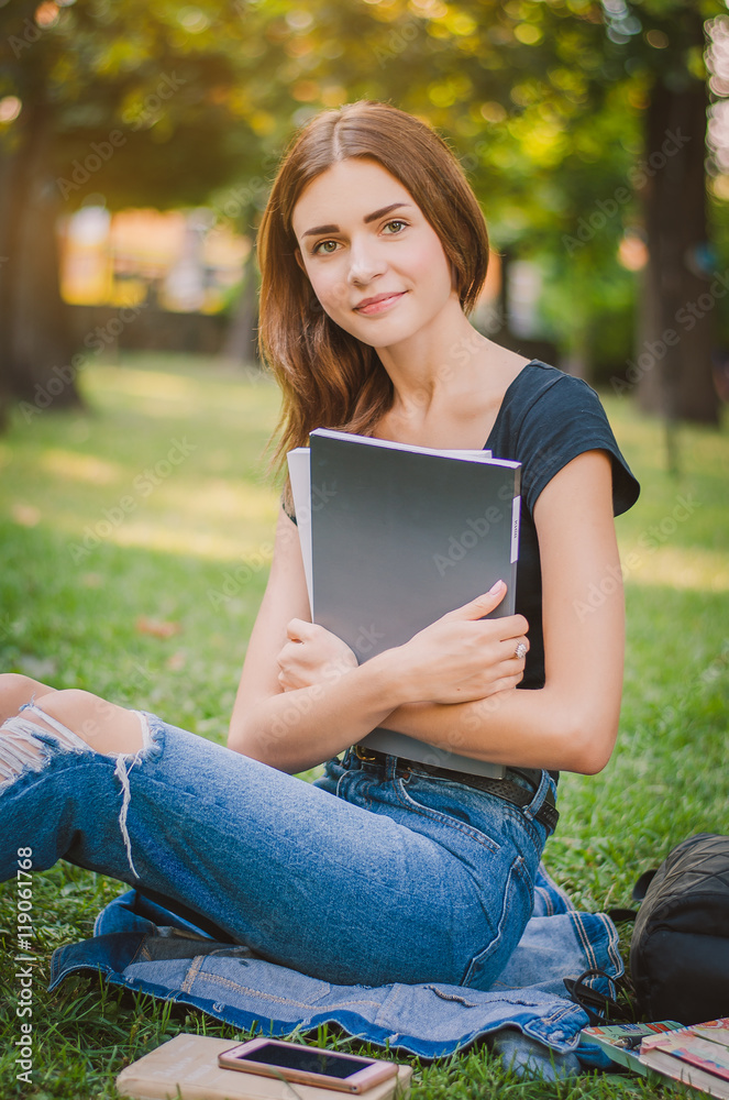 Fototapeta premium happy girl student sitting on the grass with books in their hand