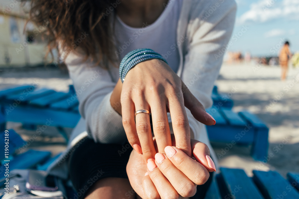 Fototapeta premium Woman with a ring on her finger sitting on a bench on the beach