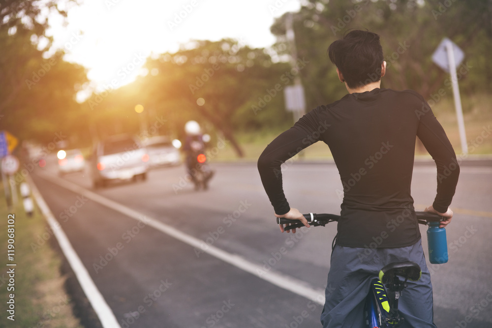 Obraz premium Cyclist riding a bike on an open road to the sunset