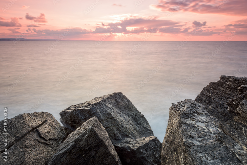 there are pink rocks near to sea with long exposure shot there are pink rocks near to sea with long exposure shot