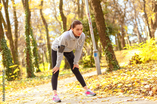 Young brunette woman catching her breath after running in park on sunny autumn day.