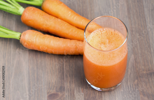 A glass of healthy carrot smoothie with carrots on wooden background. Selective focus